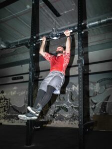 Mężczyzna w koszulce Polska wykonuje poprawne podciągnięcia na metalowym drążku na siłowni