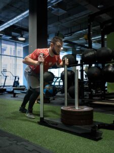 Mężczyzna w sportowej koszulce Polski pcha ciężki stojak na talerze Eleiko po siłowni