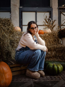 Naturalny portret kobiety w okularach opierającej głowę na dłoni, pozującej na tle siana i dyń. Spokojna, jesienna fotografia portretowa wykonana w Łodzi.