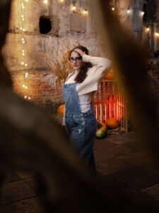 Industrialny portret kobiety na tle ceglanego muru, ciepłych światełek i dyń. Jesienna sesja zdjęciowa z wykorzystaniem klimatycznego, czerwonego oświetlenia w Łodzi.