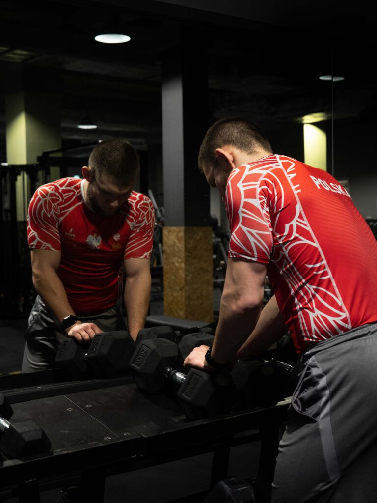 zapaśnik na siłowni z ciężkimi hantlami stojący przy lustrze - sesja portretowa Łódź